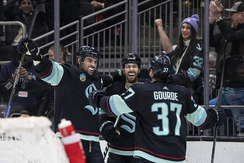 Seattle Kraken defenseman Justin Schultz (4), left, forward Oliver Bjorkstrand (22) and forward Yanni Gourde (37) celebrate an overtime goal against the Philadelphia Flyers at Climate Pledge Arena.